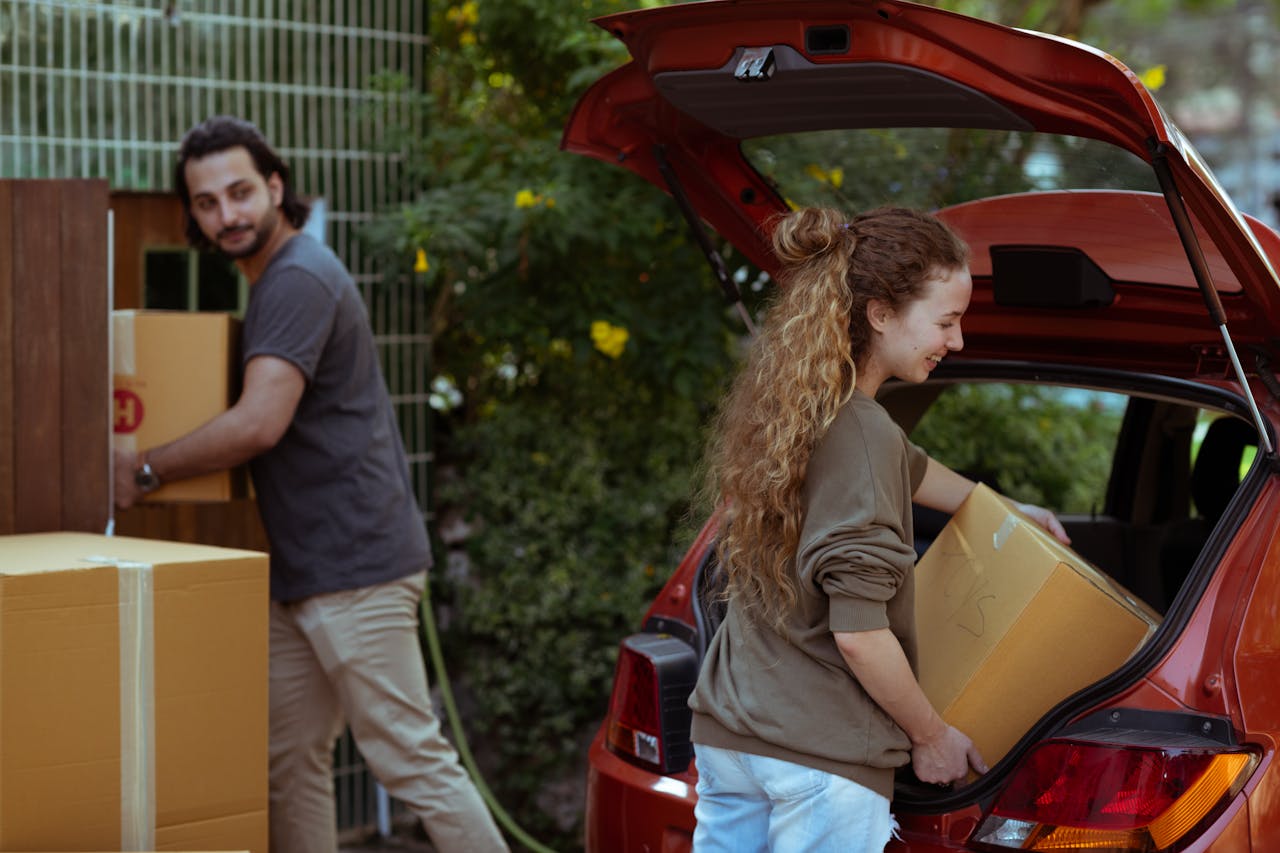 A cheerful young couple unloading boxes from a car trunk into their new home in the countryside.
